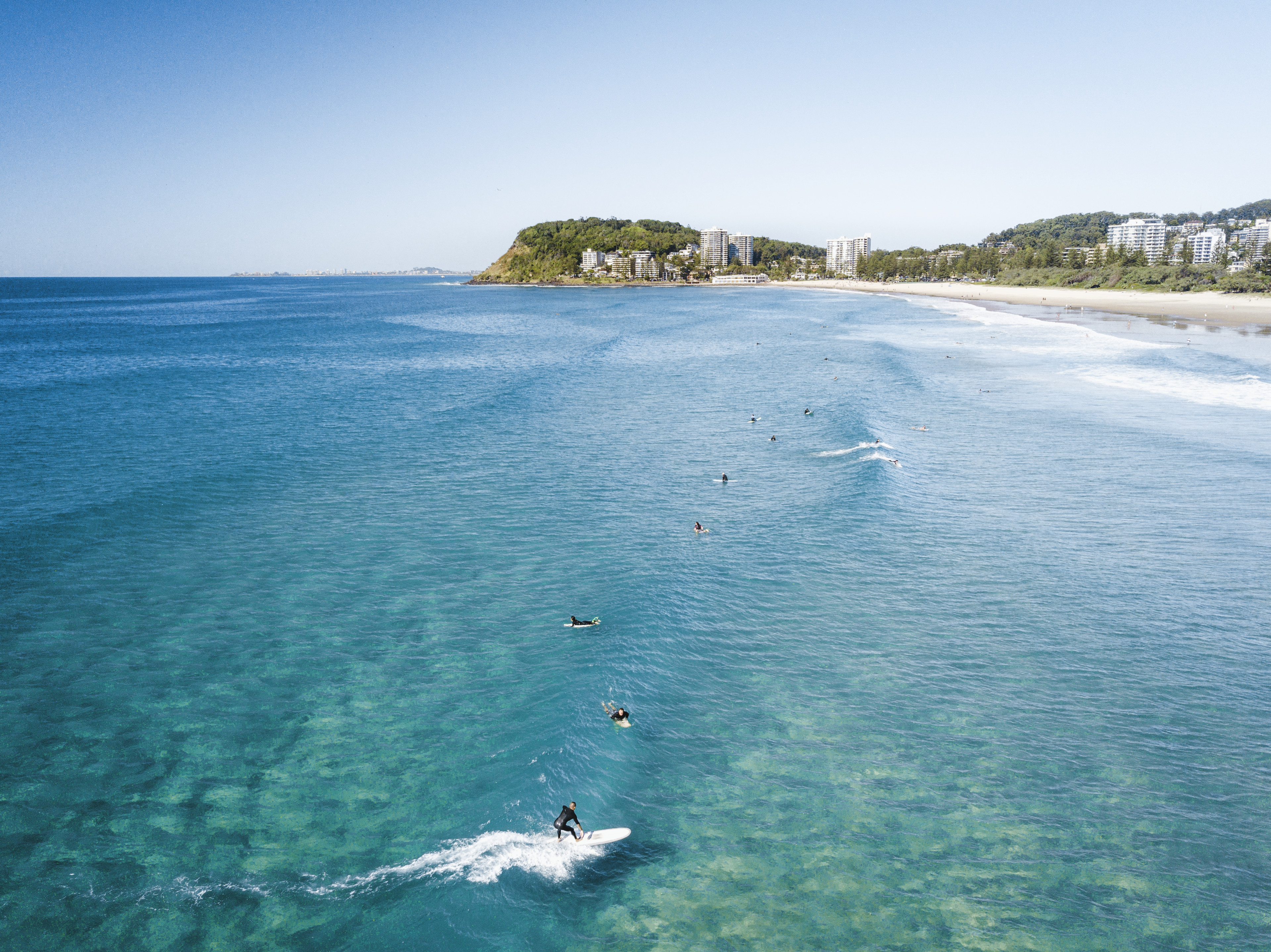 An aerial image of many surfers enjoying the vibrant blue surf of North Burleigh on the Gold Coast. Many hotels and apartment buildings can be seen in the distance. An aerial image of many surfers enjoying the vibrant blue surf of North Burleigh on the Gold Coast. Many hotels and apartment buildings can be seen in the distance.